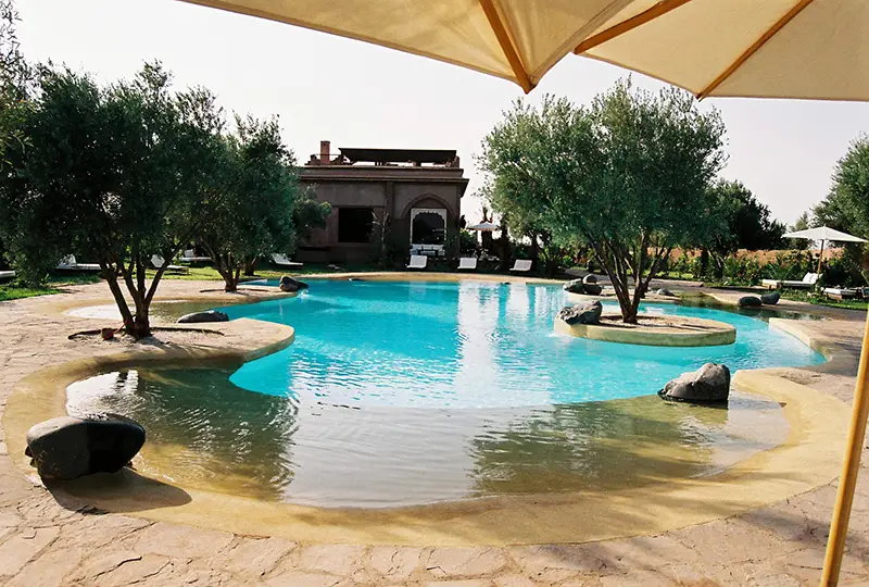 Piscine naturelle style lagon sous parasol, aménagement paysager à Marrakech, Casablanca, Rabat, Agadir, Fès, Tanger, Essaouira – Design Pool Maroc